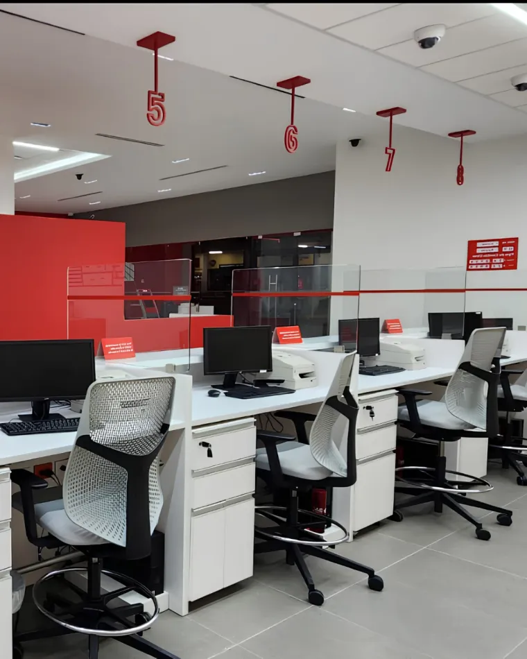 Puestos de atención con mobiliario blanco y señalización roja en la agencia BAC Credomatic de Roatán